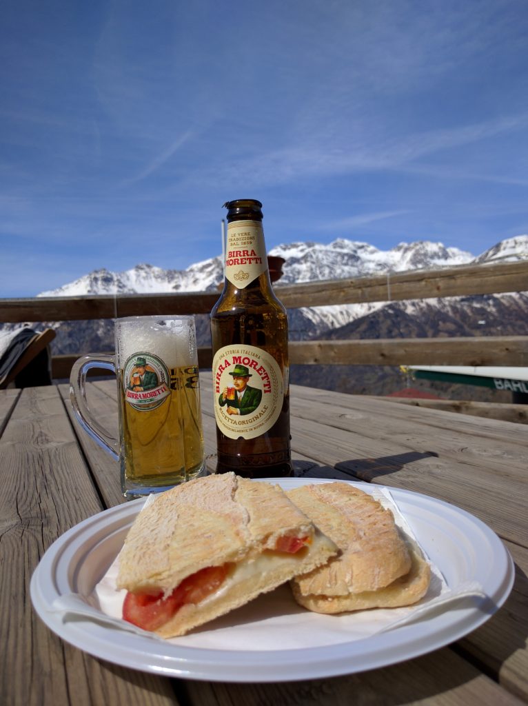 beer and sandwich on a sunny moutaintop table with snow capped alps in the background