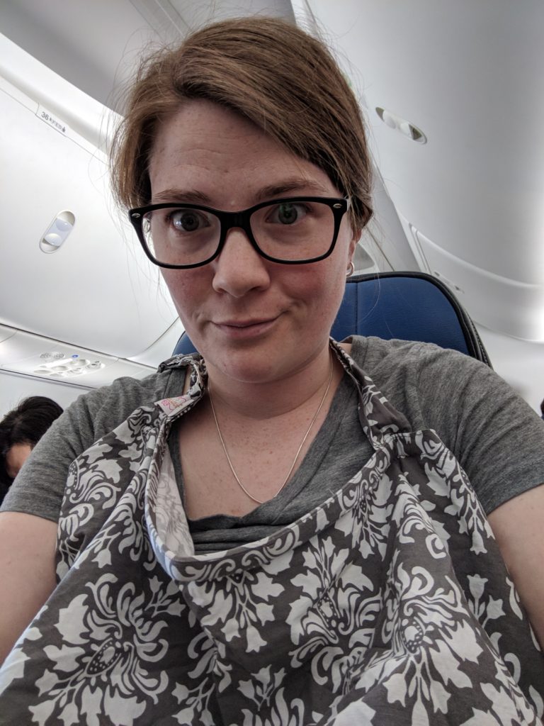 Kelly sitting on a plane, nursing cover on, pumping.