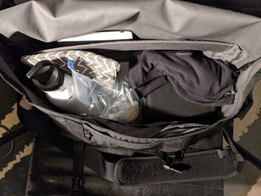 black bag opened with pump, hands free bra, cords, parts, brush. Water bottle and notebook are also visible.